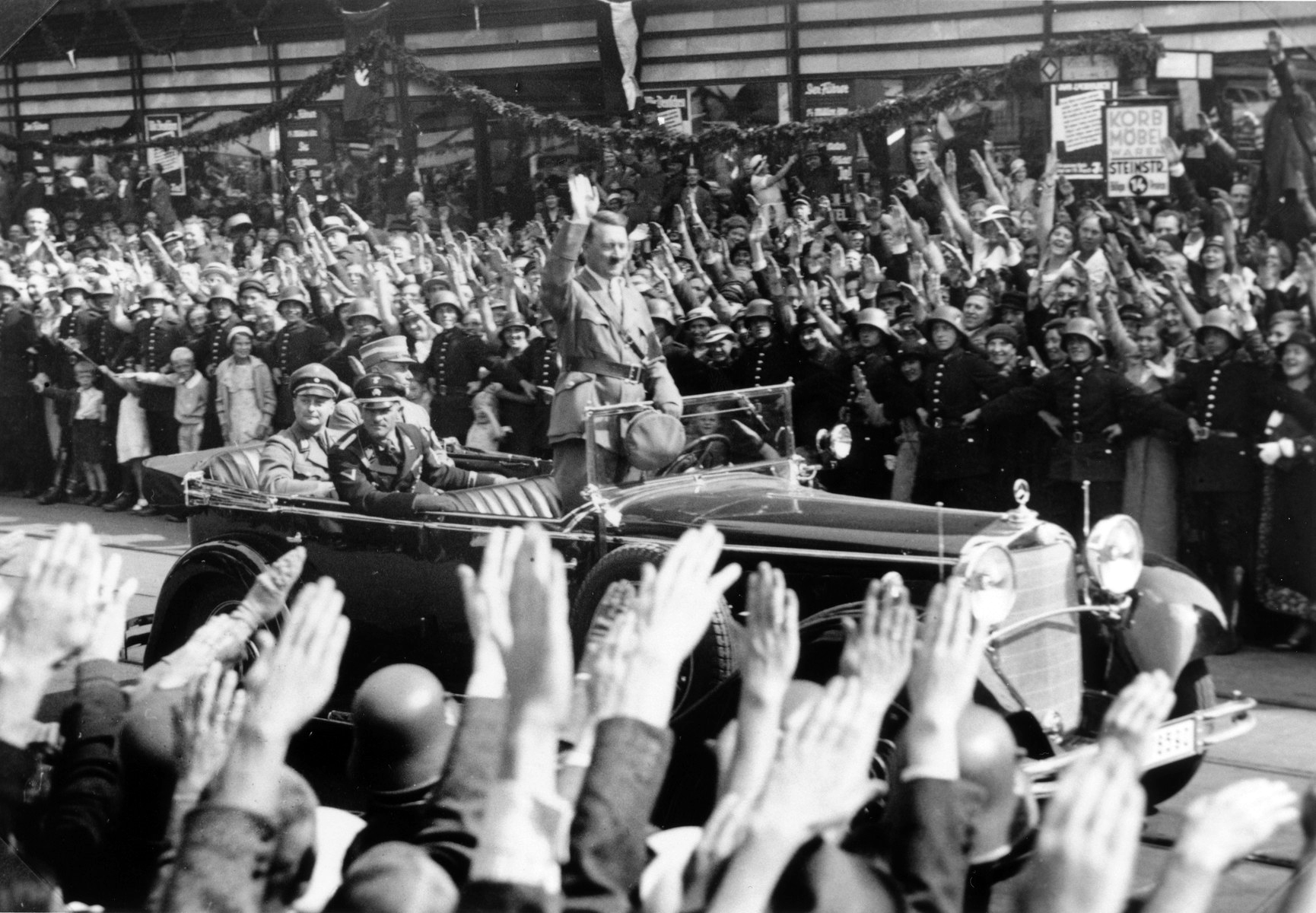 Standing in an open car, Adolf Hitler salutes a crowd lining the streets of Hamburg